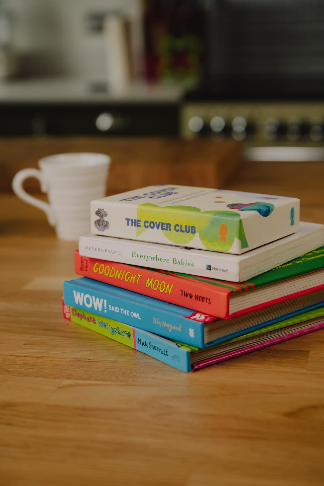 A stack of children's books with The Cover Club guide on top, beside a mug